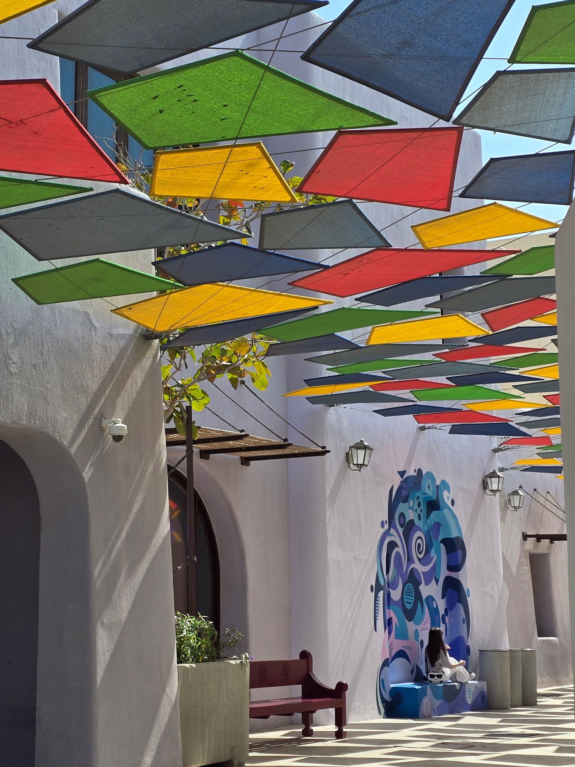Vibrant outdoor setting with colorful canopies casting shadows over modern art murals.