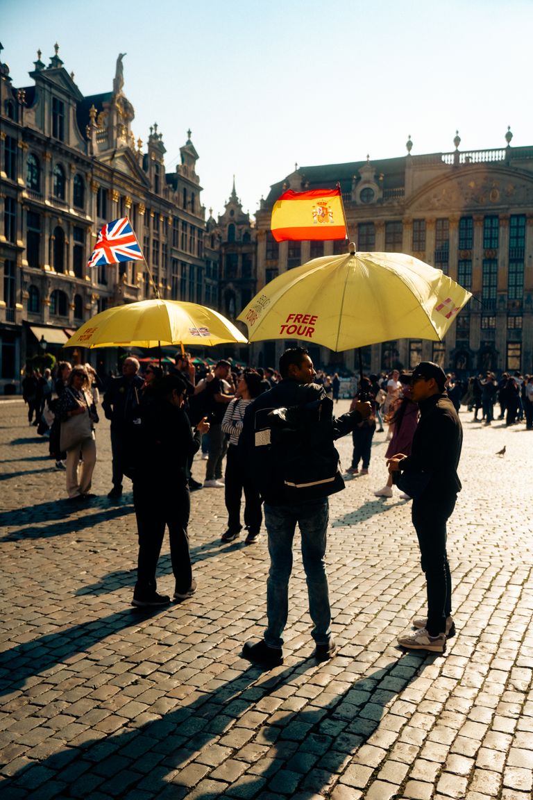 What a Good Walking Tour Helps Me See - Tourists gather under yellow umbrellas for a free tour at Brussels' historic square.
