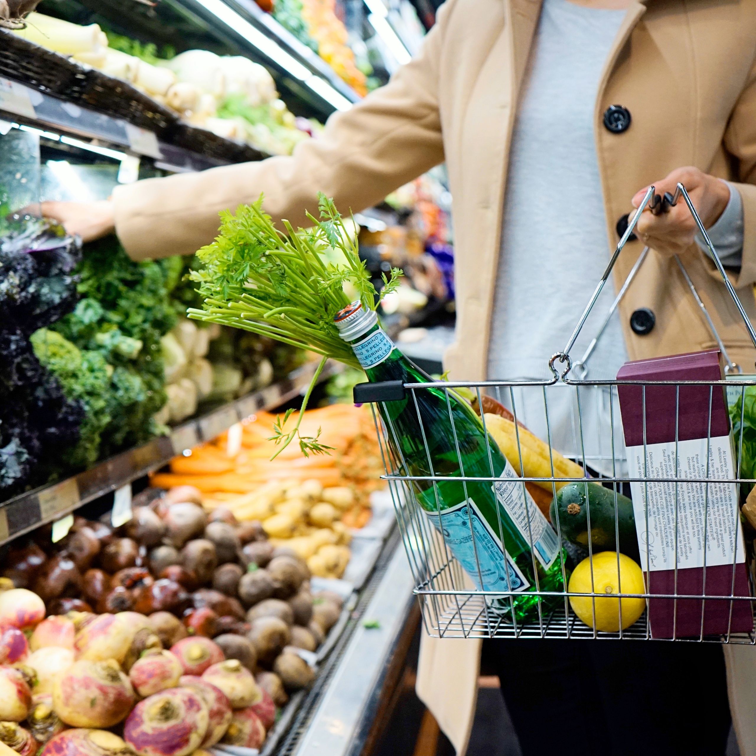 What a Grocery Receipt Reveals About the Cost of Care - Woman selecting fresh produce in a supermarket with a basket full of groceries.