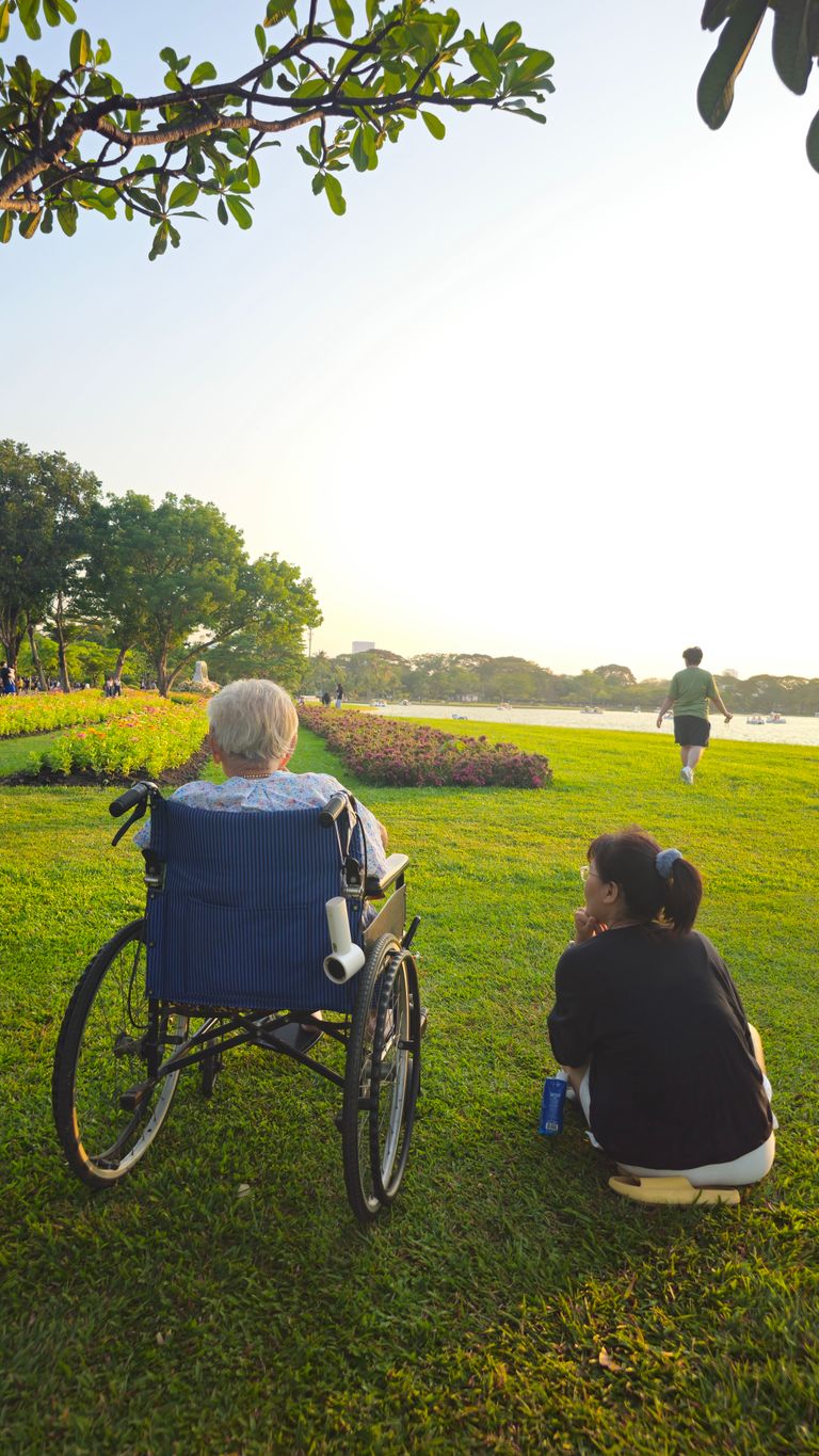 What a Park Teaches Me About Public Care - Elderly person and caregiver enjoy a serene afternoon by the river in Bangkok.