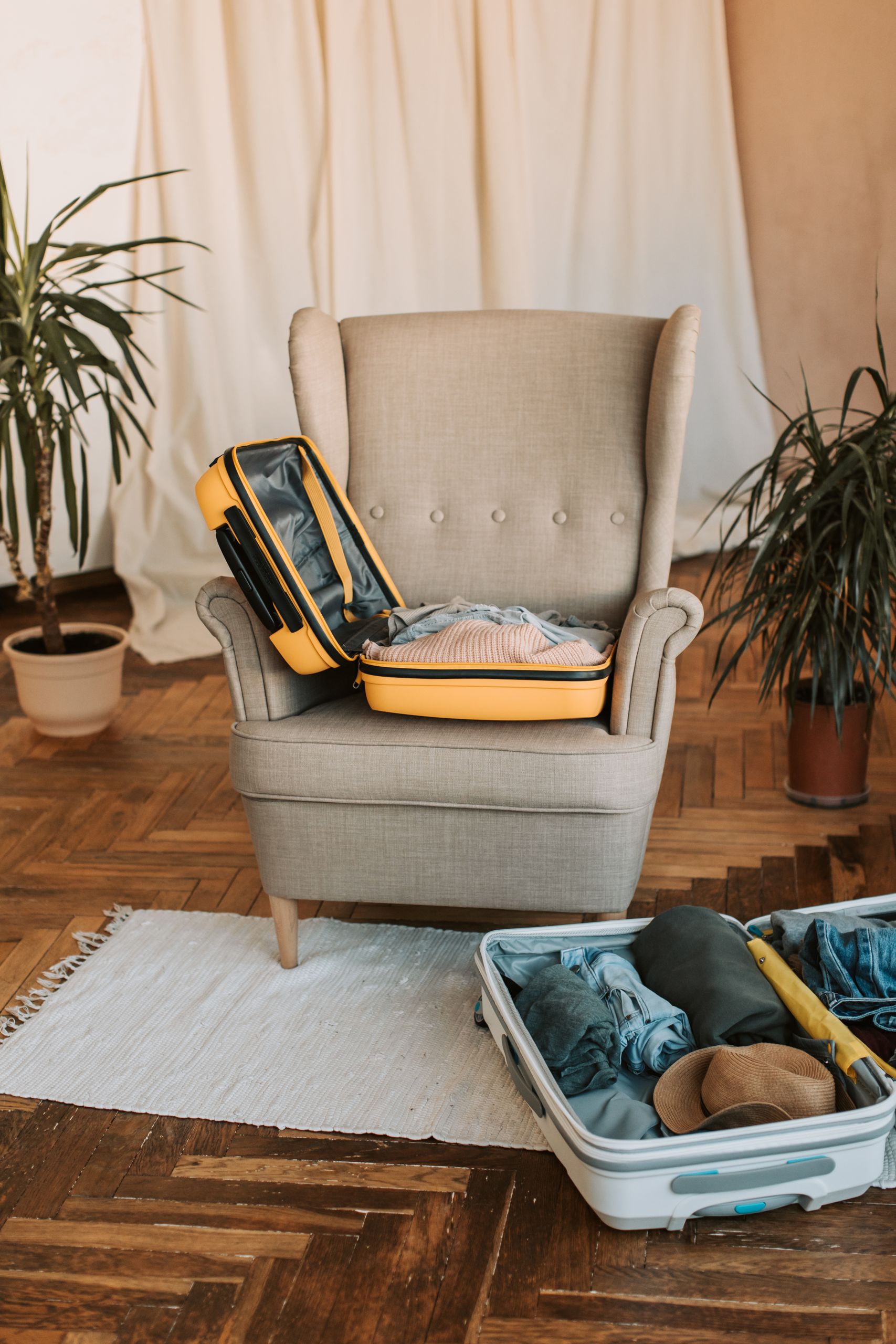What I Am Leaving Behind at the End of This Year - A comfortable chair with open suitcases beside indoor plants, ready for travel preparation.