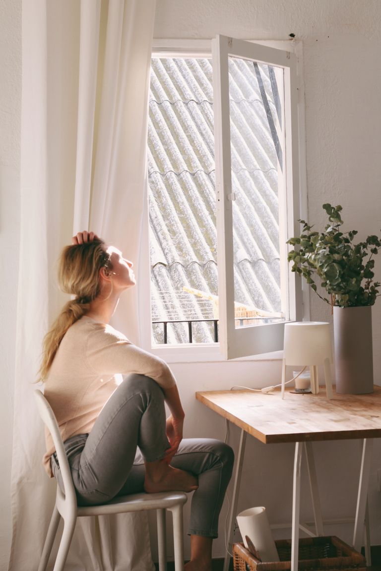 What the Window Teaches Me About Staying Still - A serene moment as a woman enjoys sunshine near a window in a cozy interior setting.
