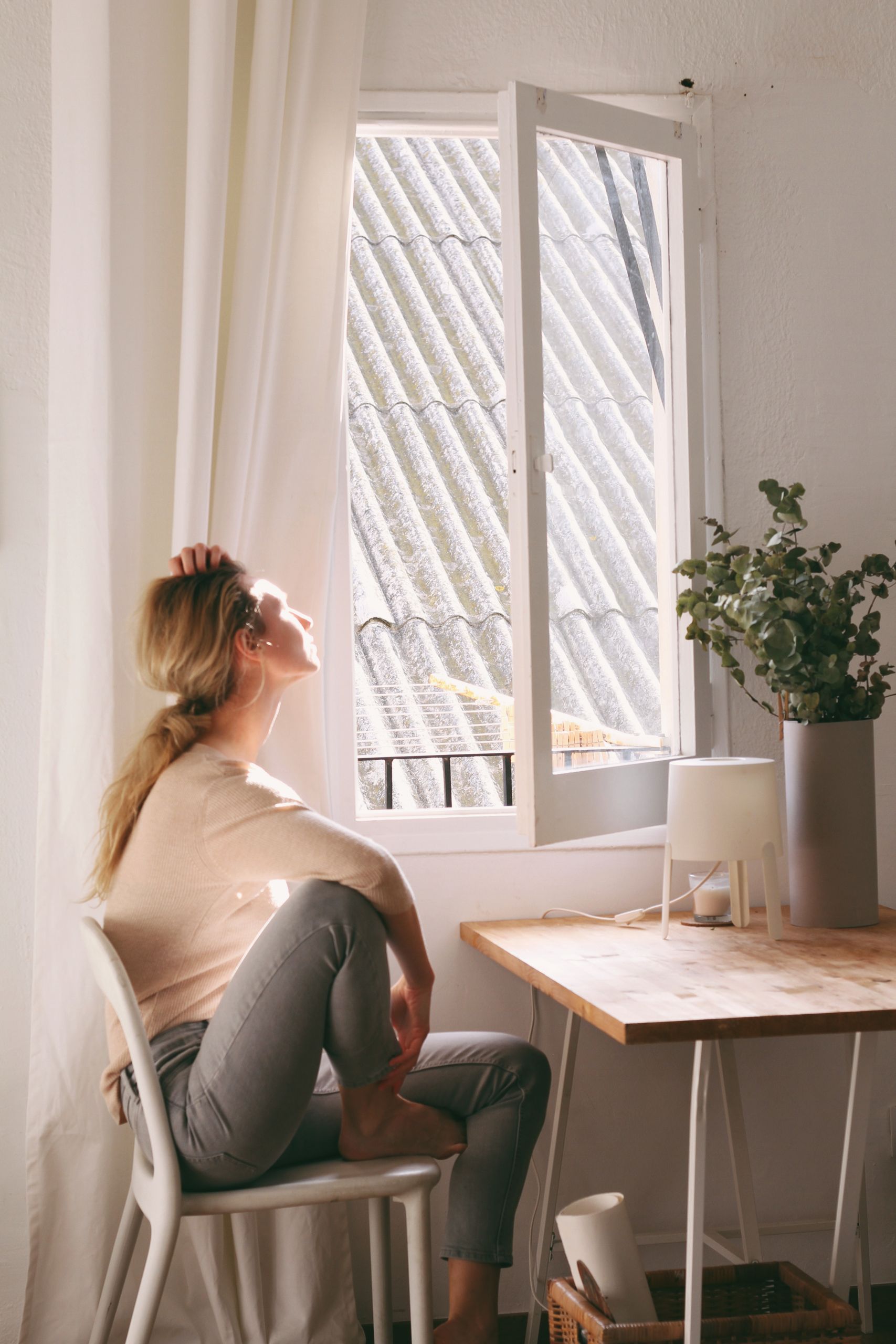 What the Window Teaches Me About Staying Still - A serene moment as a woman enjoys sunshine near a window in a cozy interior setting.