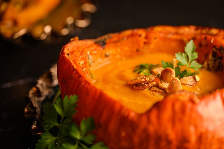 When Fall Brings Me Back to the Kitchen - Close-up of creamy pumpkin soup garnished with seeds and parsley in a pumpkin bowl.