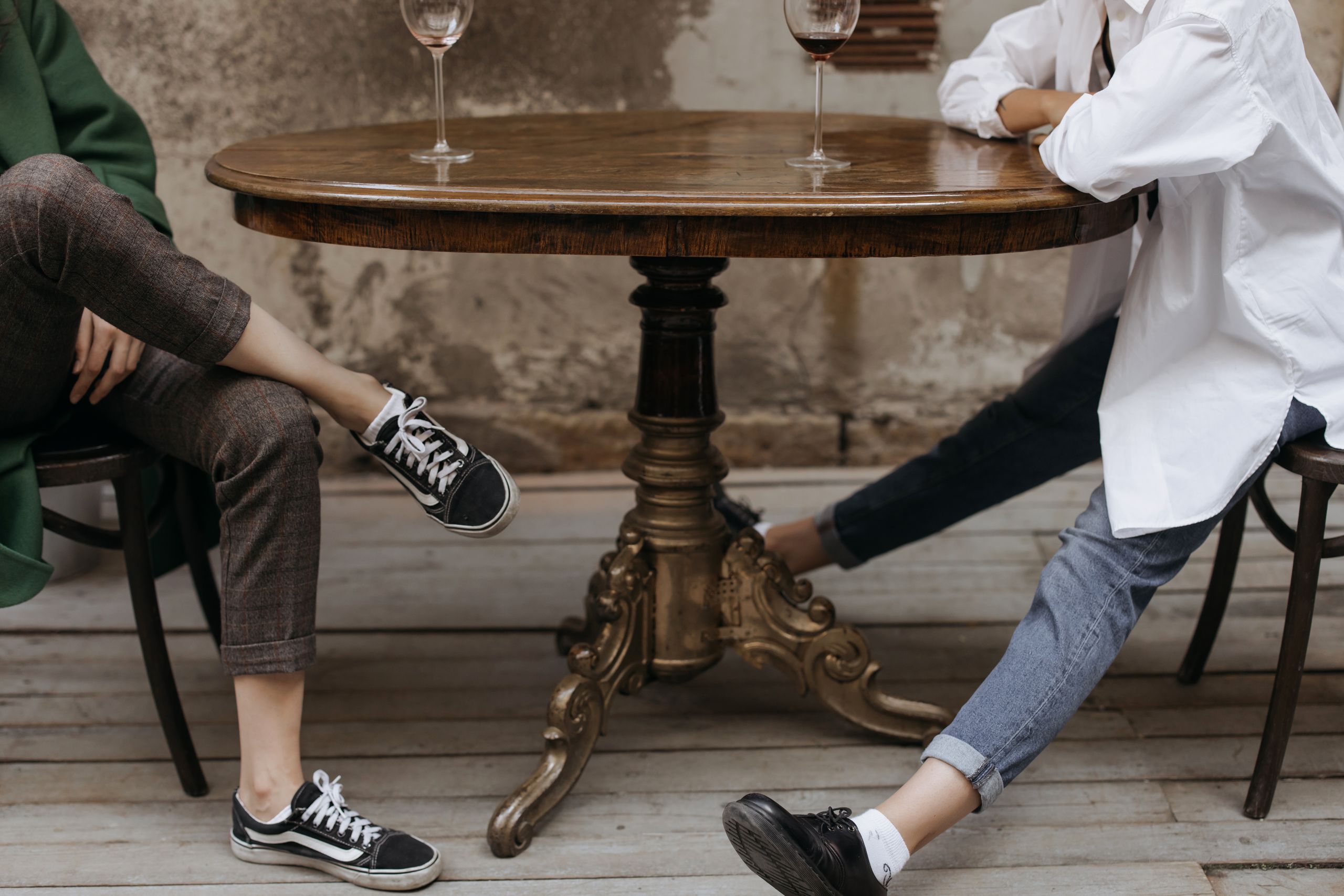 When the Table Has to Hold the Truth - Two people relax with drinks at a rustic table, showcasing casual style and ambiance.