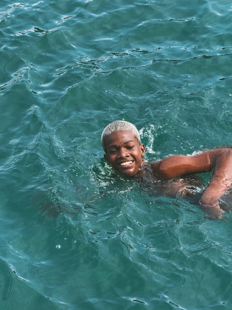 Who Says Black People Can’t Swim? - Smiling young man enjoying a swim in vibrant turquoise sea water.