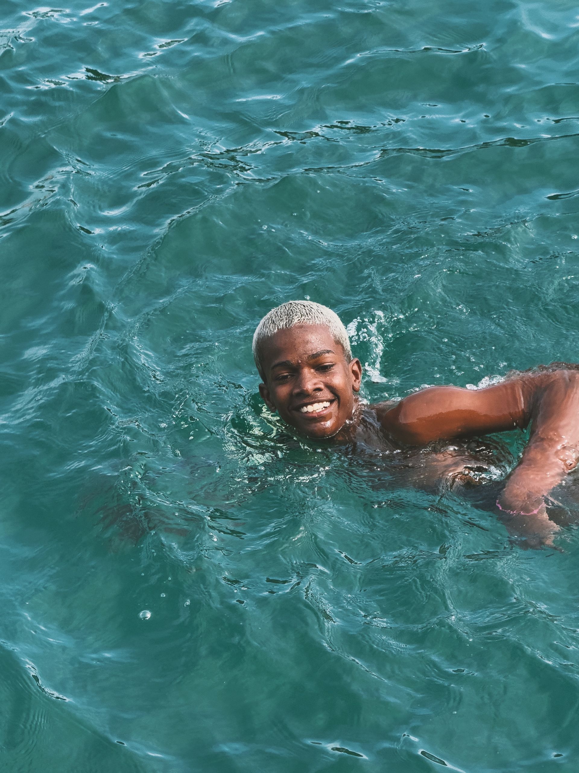 Who Says Black People Can’t Swim? - Smiling young man enjoying a swim in vibrant turquoise sea water.