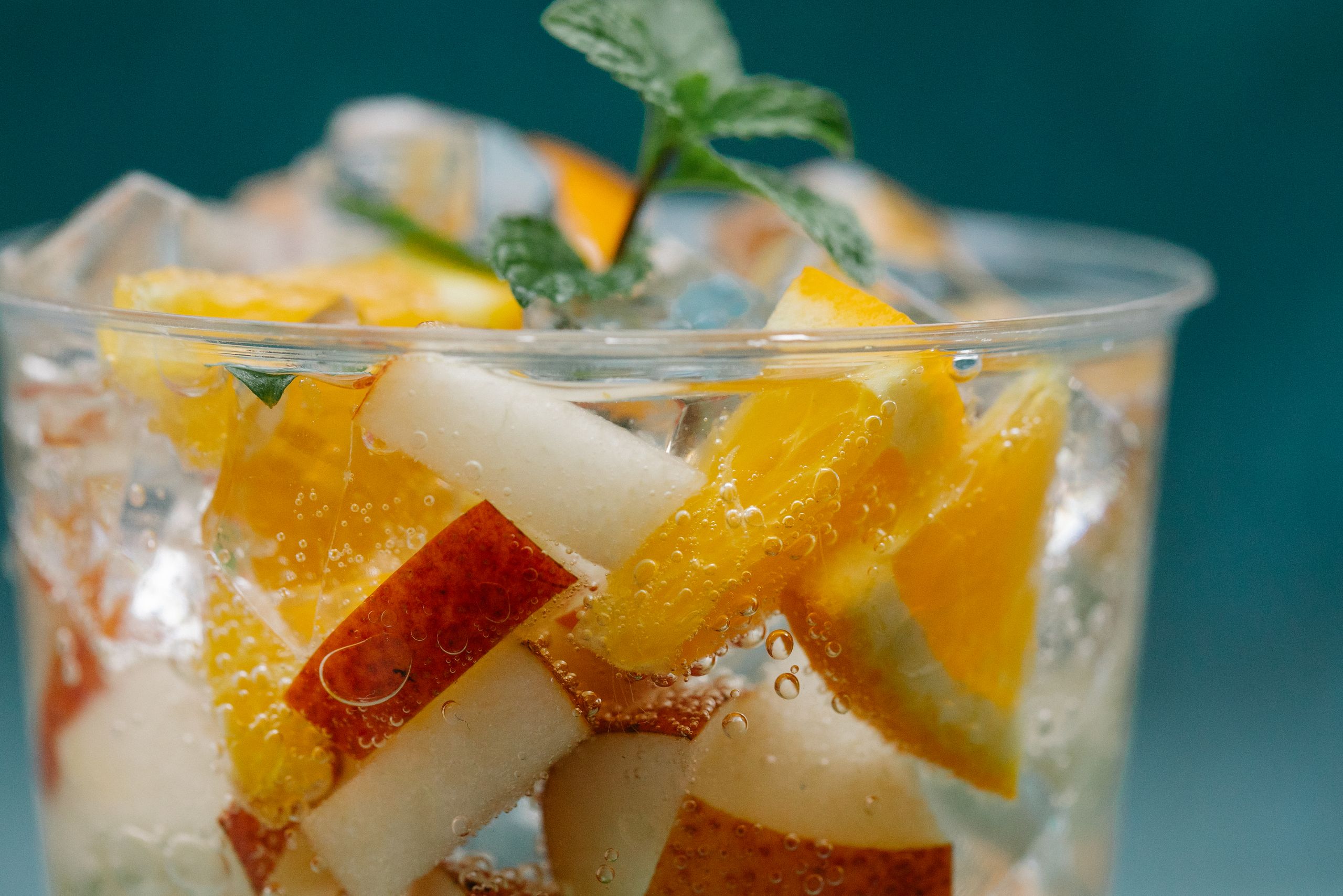 Why Cold Fruit Feels Like Summer Mercy - Close-up of a refreshing citrus and apple infused drink with ice in a cup.