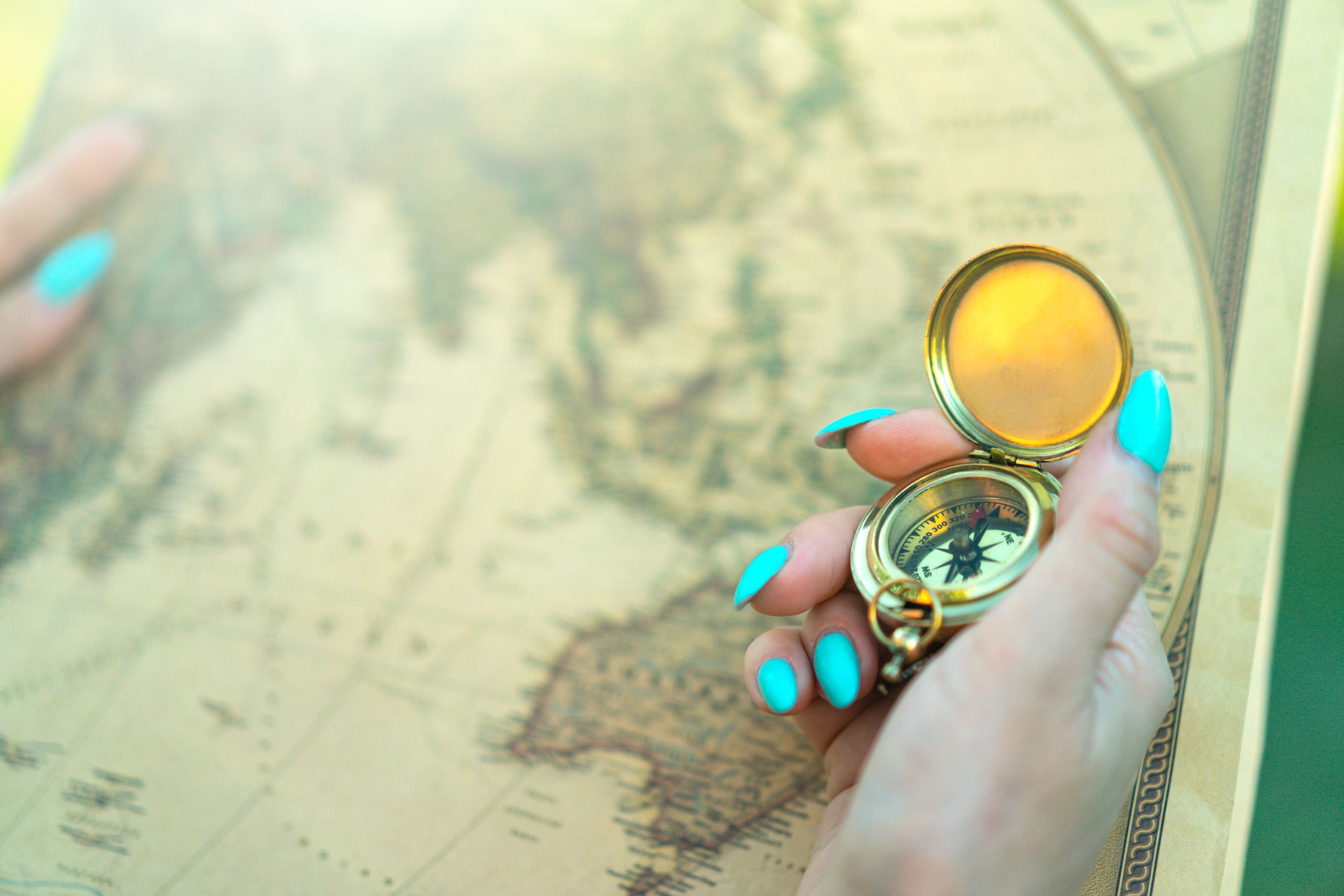Why Curiosity Is Still My Favorite Compass - Close-up of a hand holding a vintage compass over an ancient map, symbolizing exploration and travel.