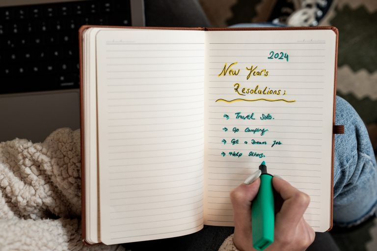 Why I Am Choosing a Smaller Kind of Resolution - Person making 2024 New Year's resolutions in a notebook with a green marker.