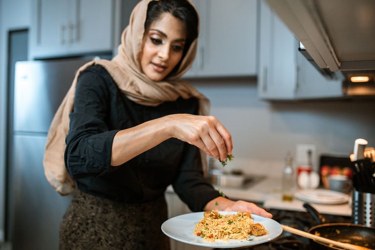 Why I Am Cooking More Meals That Feel Like Home - A woman sprinkles herbs on a rice dish, showcasing food preparation skills.