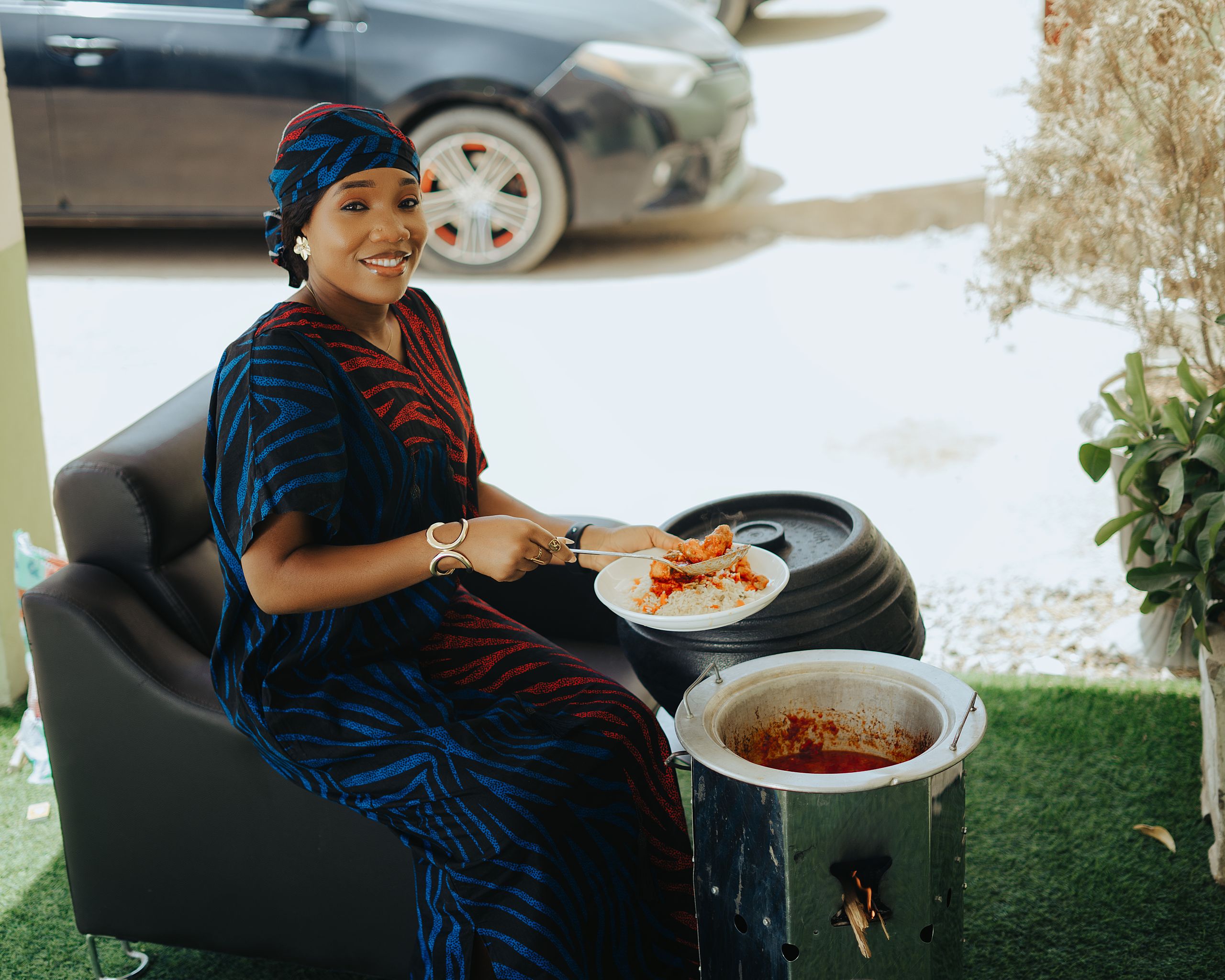 Why I Care About Who Gets Fed First- A smiling woman in vibrant attire enjoys a traditional meal outdoors, exuding happiness.