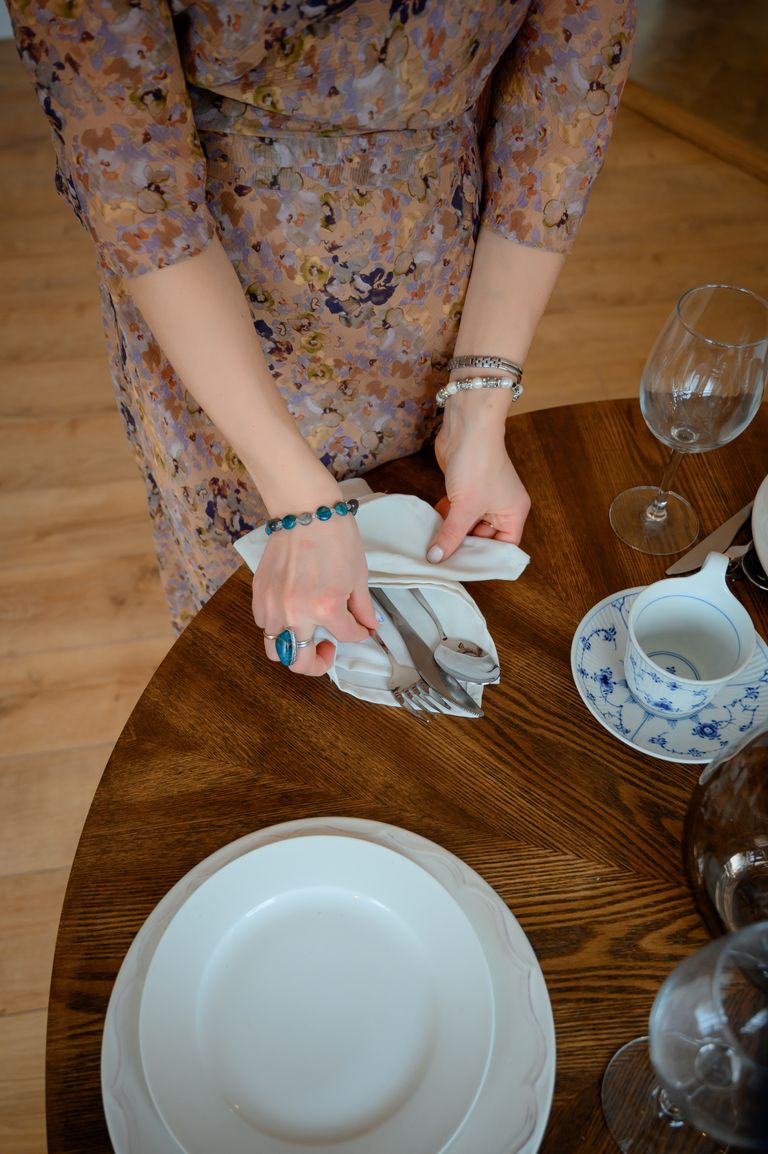 Why I Respect the Hands That Set the Table -A woman sets a beautifully arranged table with cutlery and plates, wearing a floral dress.