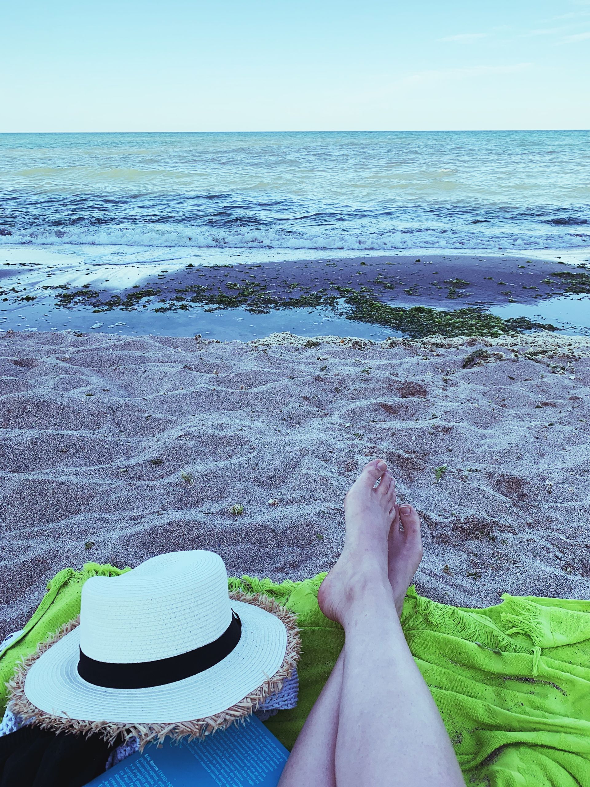 Why I Still Believe in Summer Even When It Is Complicated - Crop barefoot person with straw hat lying on green plaid on sandy shore near blue waving sea