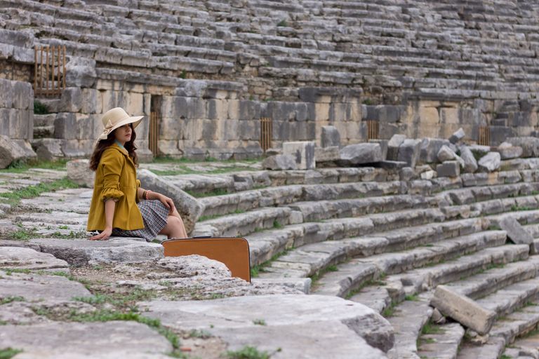 Why I Travel for Culture, Not Escape | DG Speaks - A woman in a hat and yellow jacket sitting in an ancient Turkish amphitheater.