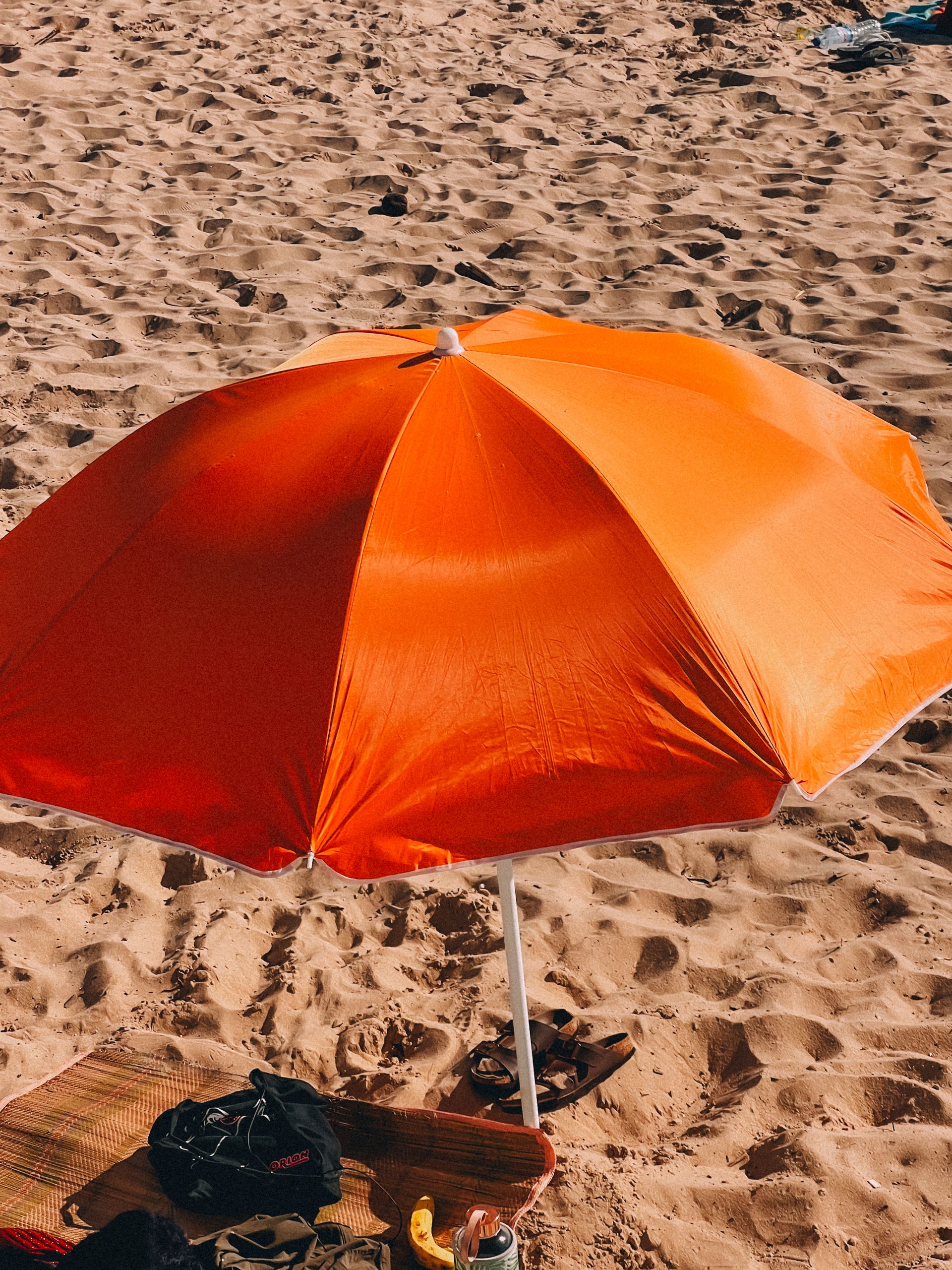 Why I Want My Summer to Have More Shade - A vibrant orange beach umbrella providing shade on a sunny, sandy beach, perfect for summer relaxation.
