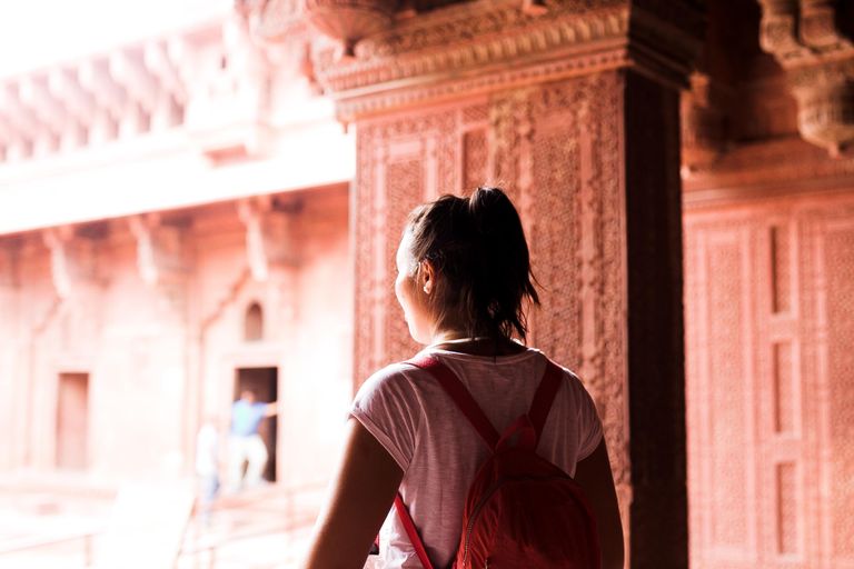 Why Solo Travel Keeps Asking Me Better Questions - Young female traveler with backpack exploring a historic site. Back view.