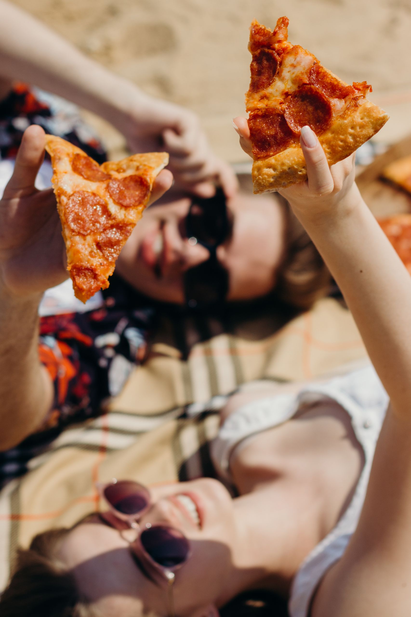 Why Summer Food Should Be a Little Messy - Two friends enjoying a sunny picnic with pepperoni pizza slices. Perfect summer outing.