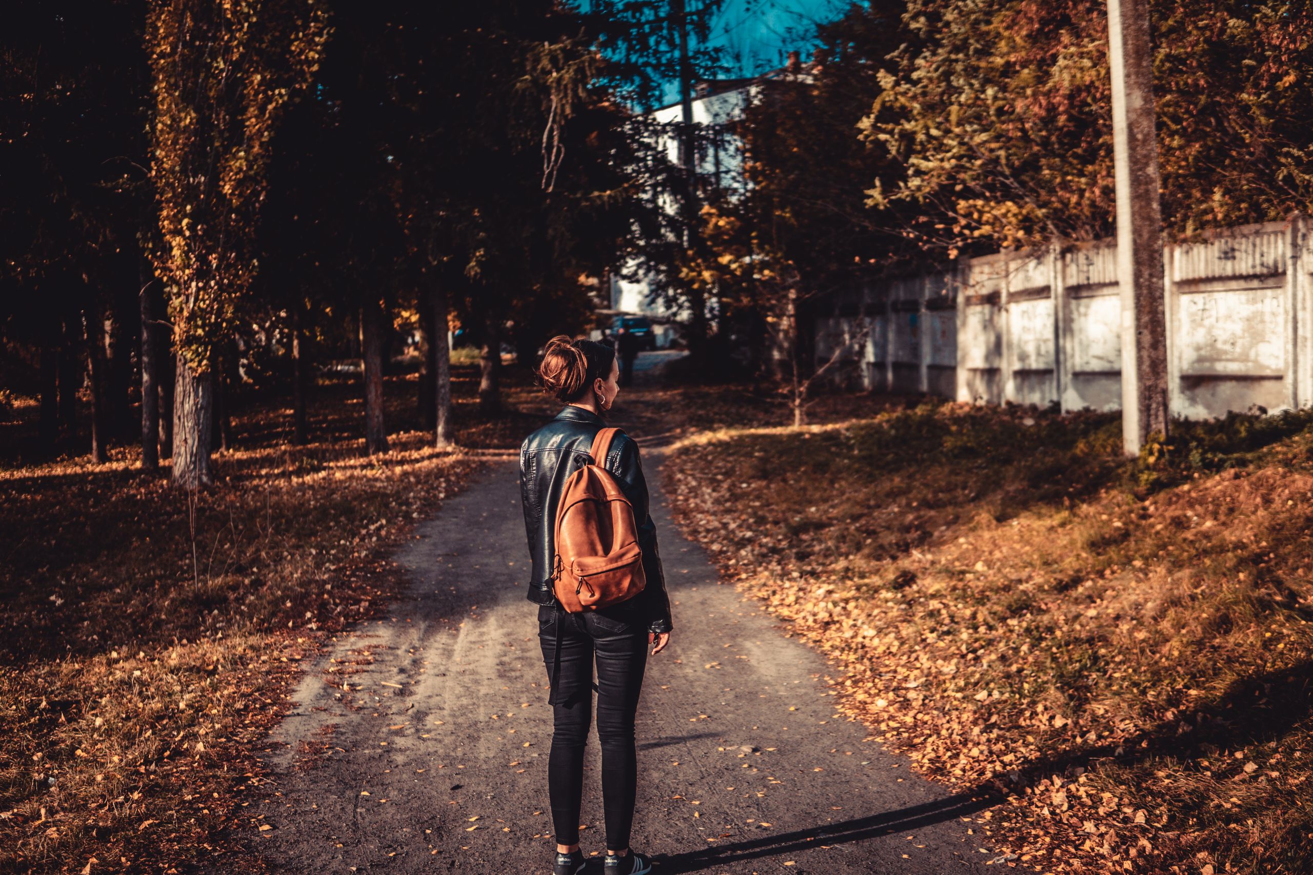 Why Walking Alone Feels Like Coming Back to Myself - A woman with a brown backpack walks down a leafy path in the fall.