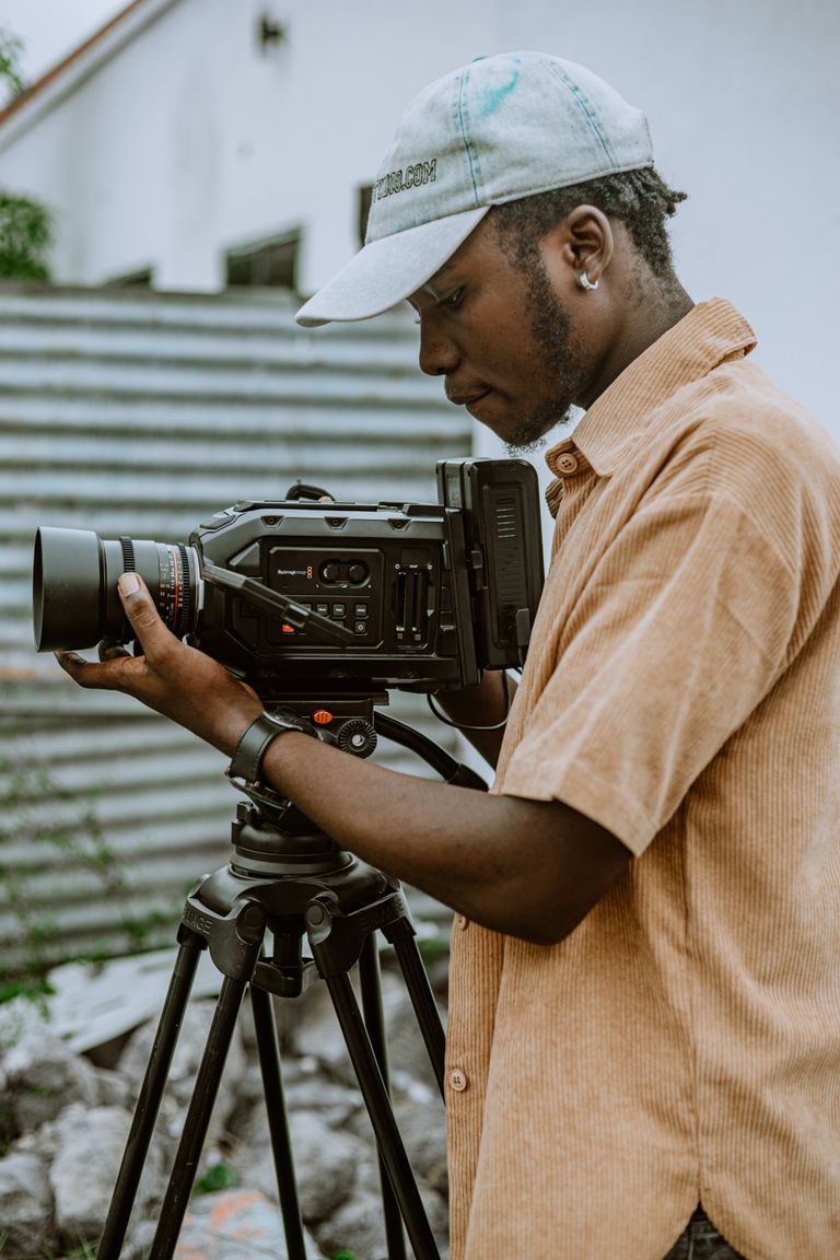 A young filmmaker adjusts a professional camera outdoors, capturing a creative moment.