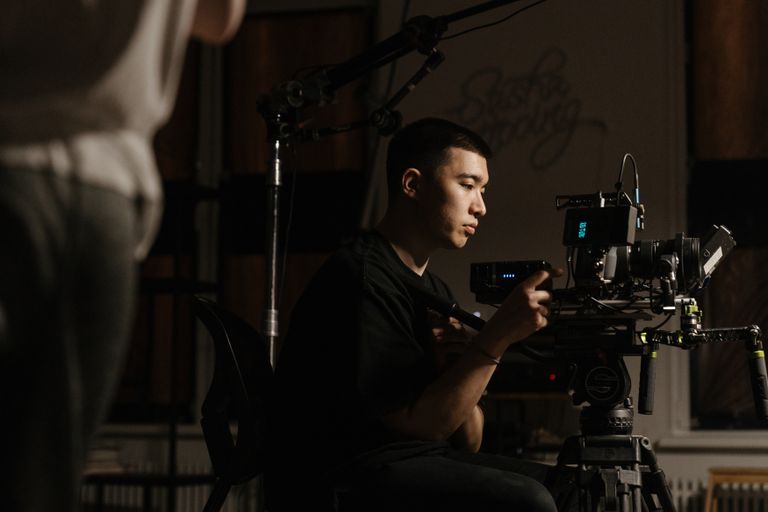 Side view of cameraman operating professional equipment during film production indoors.